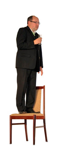 Spieler der Theatergruppe Hinterbrühl steht am Sessel und hält ein Glas in der Hand